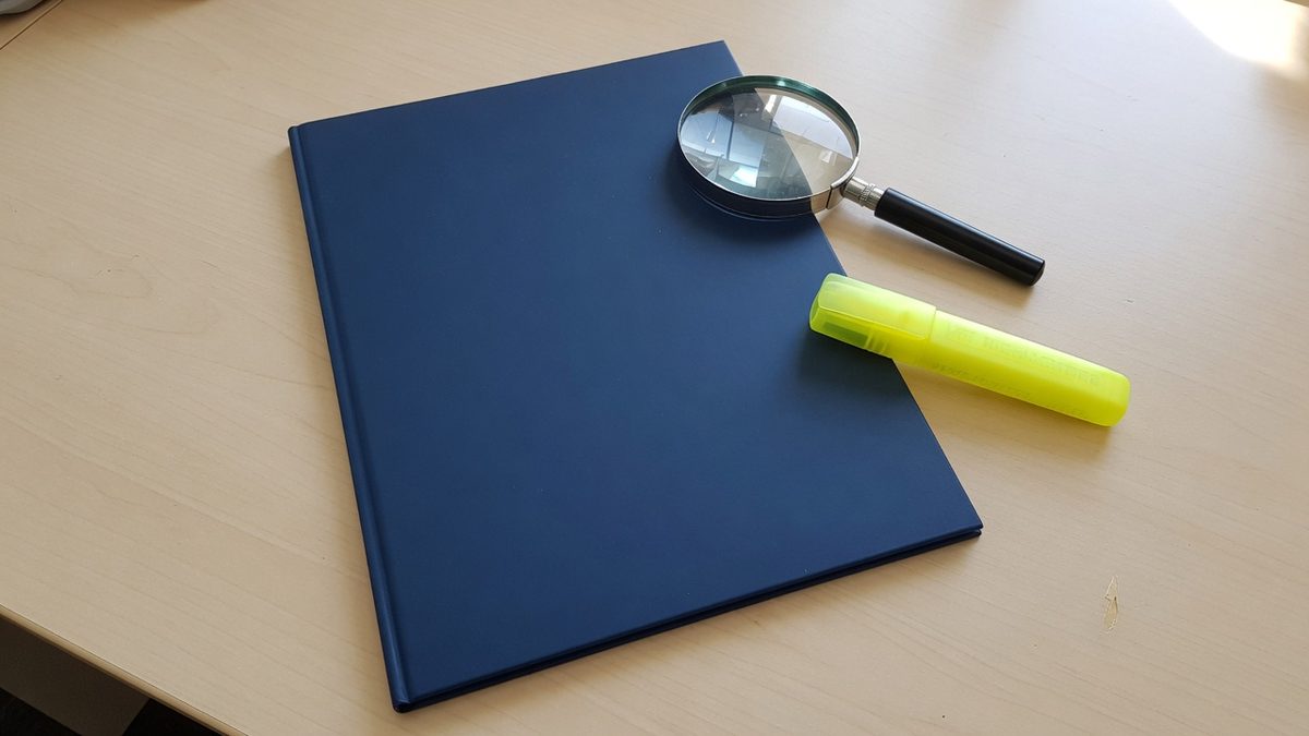 Vergrootglas boven een document met kleine lettertjes en een gele markeerstift ernaast
