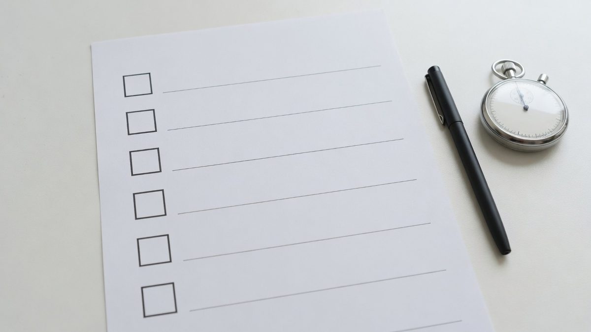 Papieren checklist met zes lege vakjes naast een pen en een stopwatch op een licht bureau